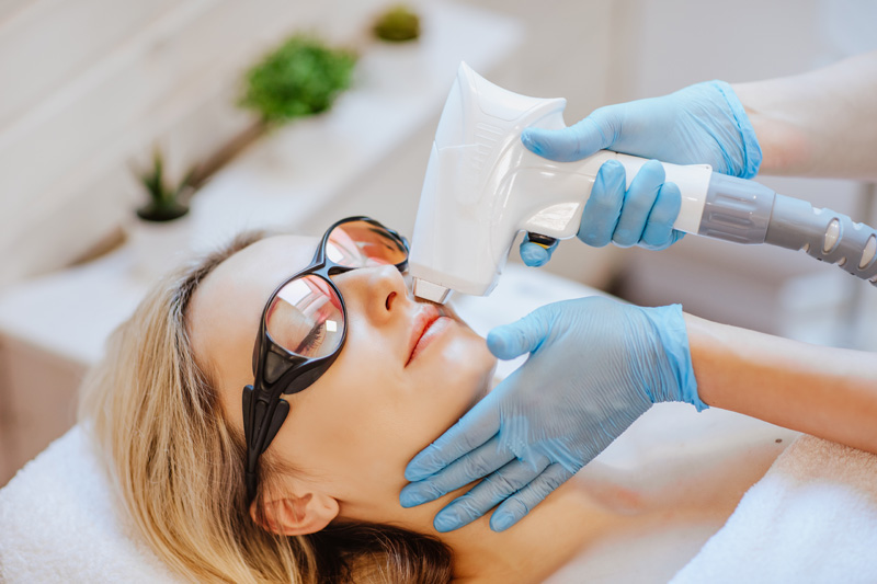 doctor s hands in blue medical gloves using the hair removal machine on the patient s face